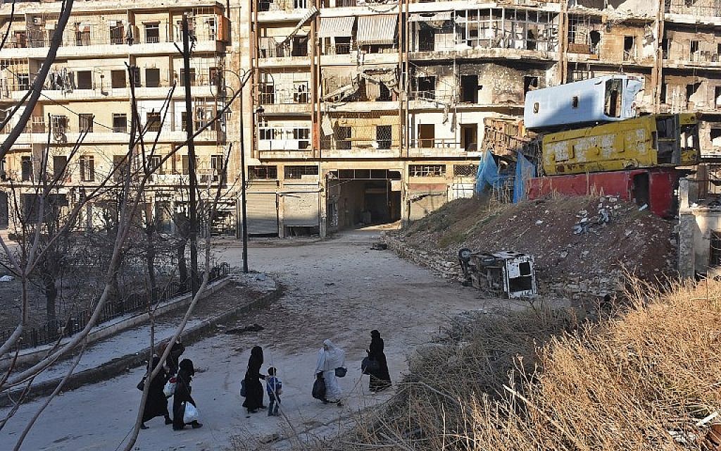 Syrian residents fleeing the violence in the eastern rebel-held parts of Aleppo walk past a makeshift barricade made of wreckages of buses as they evacuate from their neighbourhoods through the Bab al-Hadid district after it was seized by the government forces, on December 7, 2016. (AFP/GEORGE OURFALIAN)