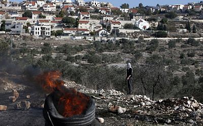 A Palestinian protester looks at burning tires during clashes with Israeli security forces near the settlement of Kedumim in the West Bank on December 9, 2016. (AFP/JAAFAR ASHTIYEH)