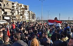 A man holds a Syrian flag bearing the portrait of President Bashar Assad as residents in a government-held area of Aleppo gather in the street during an evacuation of rebel fighters and their families on December 15, 2016. (AFP/George Ourfalian)