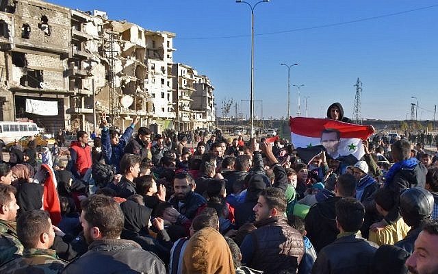 A man holds a Syrian flag bearing the portrait of President Bashar Assad as residents in a government-held area of Aleppo gather in the street during an evacuation of rebel fighters and their families on December 15, 2016. (AFP/George Ourfalian)