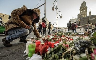 A mourner places a candle on December 21, 2016, at a makeshift memorial near the Kaiser Wilhelm Memorial Church in Berlin, close to the site where a truck crashed into a Christmas market two days before. (AFP Photo/Clemens Bilan)