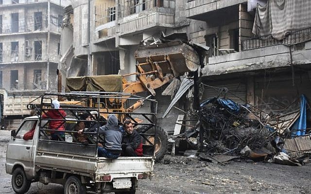 Syrian civilians drive past a tractor removing rubble as the Syrian government starts to clean up areas formerly held by opposition forces in the northern city of Aleppo on December 27, 2016, in the Shaar district. (AFP/George Ourfalian)
