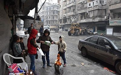 Syrian children gather around a fire as the Syrian government starts to clean up areas formerly held by opposition forces in the northern city of Aleppo on December 27, 2016, in the Shaar district. (AFP/George Ourfalian)