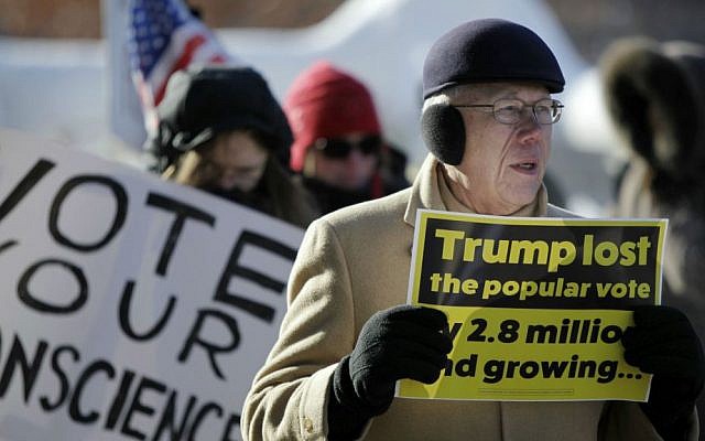 Dwayne Block of Oconomowoc, Wisconsin, marches with a sign outside of the State Capitol hours before the Electoral College votes in Madison, Wisconsin, Monday, Dec. 19, 2016. (Michael P. King/Wisconsin State Journal via AP)
