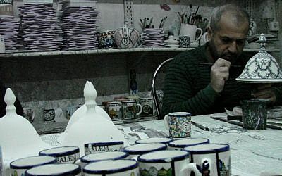 Loa'i Ghaithe carefully applies gold trim to a specialty item. (Brett Kline/Times of Israel)