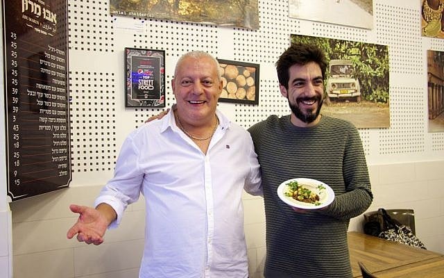 Matan Abrahams, who is the head chef at the Hudson Brasserie, a high-end Steakhouse in Tel Aviv, stands with Issa Maron on November 30, 2016, holding their shared creation of the first-ever hummus and slow-cooked barbecued mix. (Dov Lieber / Times of Israel)