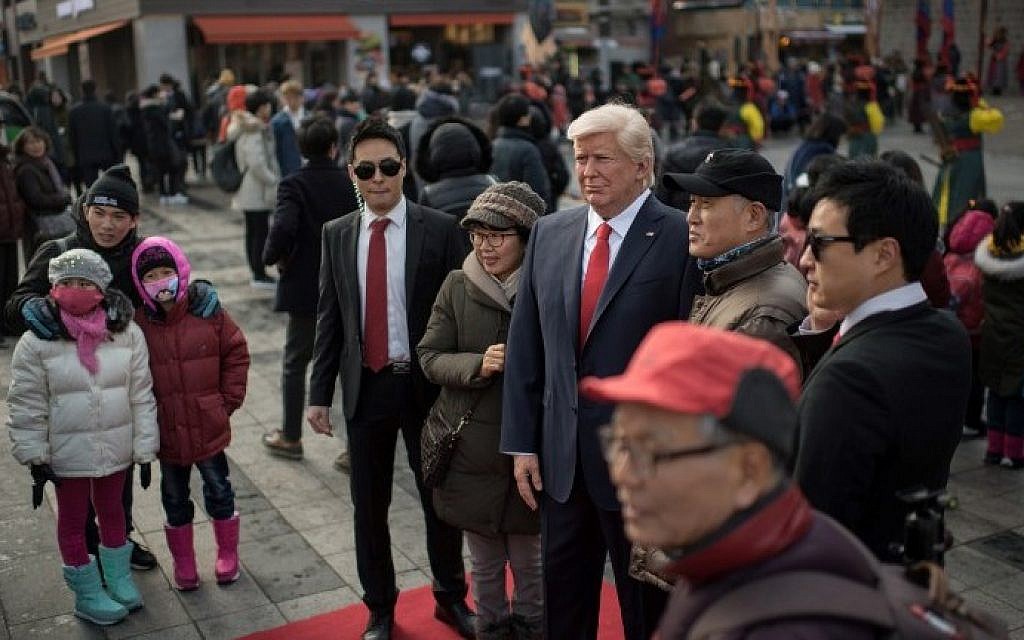 Pedestrians pose with a waxwork figure of US President-elect Donald Trump is prepared to be placed on a street after it was unveilied at the Grevin waxwork museum in Seoul on January 20, 2017. (AFP PHOTO / Ed JONES)