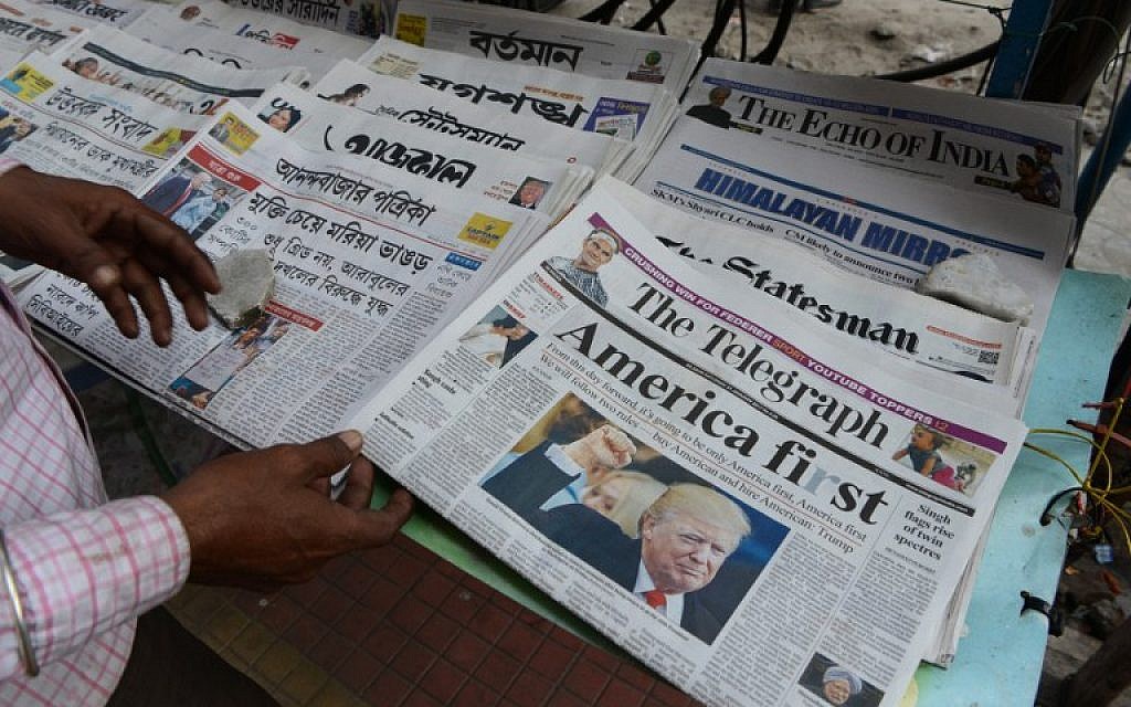 An Indian man reads a newspaper carrying front page news of the inauguration of US President Donald Trump, at a newspaper stand in Siliguri on January 21,2017. (AFP PHOTO / Diptendu DUTTA)