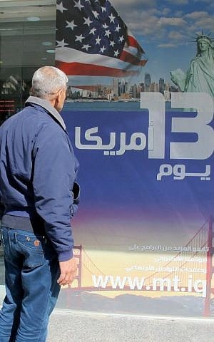 An Iraqi man stands next to an ad for a 13-day trip to the US at a travel agency in Baghdad on January 28, 2017, a day after Donald Trump signed a new executive order to suspend refugee arrivals and impose tough controls on travelers from seven mainly-Muslim countries, including Iraq. (AFP PHOTO/SABAH ARAR)