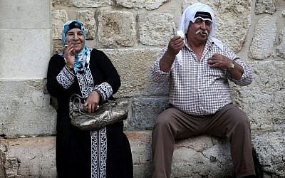 An Arab man and woman seen smoking cigarettes as they sit near the steps outside of the Church of the Holy Sepulchre in Jerusalem's Old City. November 18, 2013. (Nati Shohat/Flash90)