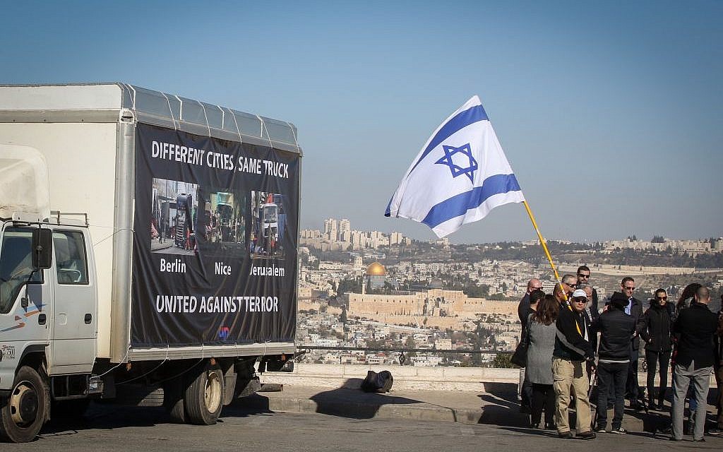 Participants in a support rally carry the Israeli flag as they walk past a truck showing images from terror attacks in Berlin, Nice and Jerusalem, all carried out using trucks as lethal weapons, near the site of the Jerusalem attack on January 11, 2017. (FLASH90)