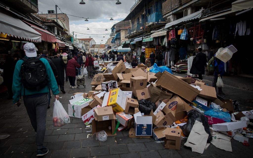 People walk past piles of garbage caused by a strike of the Jerusalem municipality at the Mahane Yehuda Market in Jerusalem, on January 29, 2017. (Yonatan Sindel/Flash90)