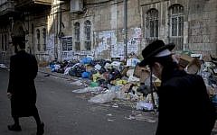 Ultra-Orthodox men walk past piles of garbage caused by a strike of the Jerusalem municipality, in Jerusalem's Mea Shearim neighbourhood, on January 30, 2017.(Yonatan Sindel/Flash90)