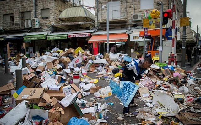 People walk past piles of garbage caused by a strike of the Jerusalem municipality, at the Mahane Yehuda Market in Jerusalem, on January 31, 2017. (Yonatan Sindel/Flash90)