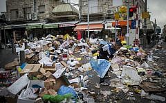 People walk past piles of garbage at the Mahane Yehuda Market in Jerusalem, caused by a strike of the Jerusalem municipality, January 31, 2017. (Yonatan Sindel/Flash90)