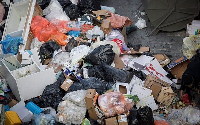 People walk past piles of garbage caused by a strike of the Jerusalem municipality, in Central Jerusalem, on January 31, 2017. (Yonatan Sindel/Flash90)