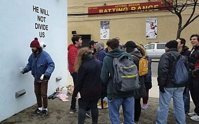 Actor Shia LeBeouf, left, stands in front of a live-steam camera with the words "HE WILL NOT DIVIDE US" posted on a wall outside of the the Museum of the Moving Image as members of the public join LeBeouf in chanting the words "He will Not Divide Us" in the Queens borough of New York, January 2017. (AP Photo/Deepti Hajela)