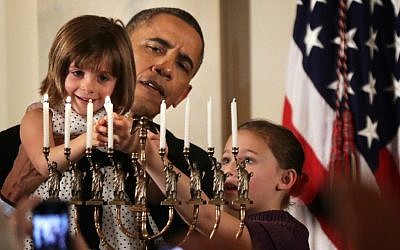 President Barack Obama holding up Kylie Schmitter, 4, to light a menorah as Kylie’s sister, Lainey, looks on during a Hanukkah reception at the White House, December 5, 2013. (Alex Wong/Getty Images)
