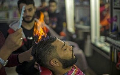 A client sits in a hair salon as barber Ramadan Edwan performs a technique that utilises fire to straighten his hair, in the Rafah refugee camp, in the Gaza Strip on February 1, 2017. (Mahmud Hams/AFP)