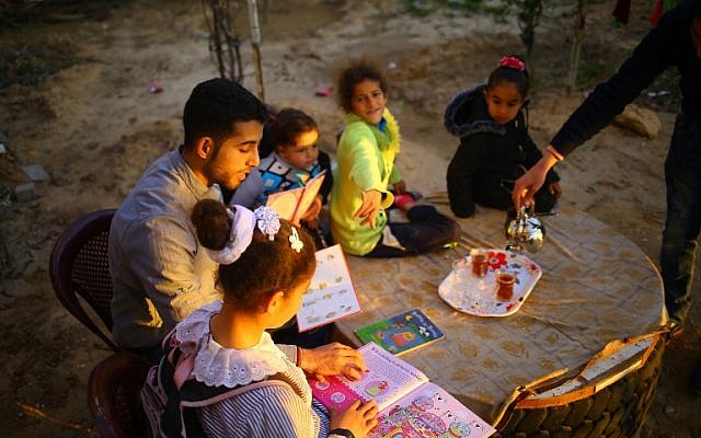 Mossab Abo Toha, who is collecting english books for his "Library and Bookshop for Gaza" project, reads english books with children in the garden at his family home in Beit Lahia in northern Gaza on February 20, 2017. (AFP Photo/Mohammed Abed)