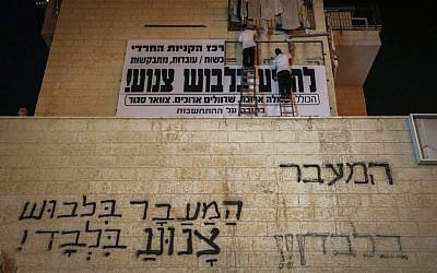 Ultra-Orthodox Jews hang modesty signs above grafitti writing where other such signs have been removed in the city of Beit Shemesh on April 19, 2016. (Yaakov Lederman/Flash90)