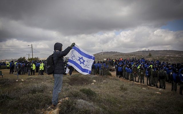 A man holds Israeli flag as Israeli security forces gather ahead of the evacuation of the illegal outpost of Amona, on February 1, 2017. (Miriam Alster/Flash90) A man holds Israeli flag as Israeli security forces gather ahead of the evacuation of the illegal outpost of Amona, on February 1, 2017. (Miriam Alster/Flash90)