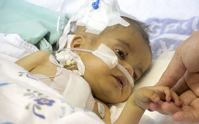 Yacub, a two-year-old Afghan, on February 23, 2017, holds the hand of the Israeli heart surgeon who saved his life. (Dov Lieber/Times of Israel)