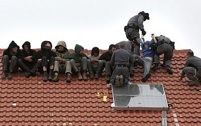 Israeli police remove protesters from the roof of a home slated to be destroyed in the West Bank settlement of Ofra on March 1, 2017. (AFP Photo/Menahem Kahana)