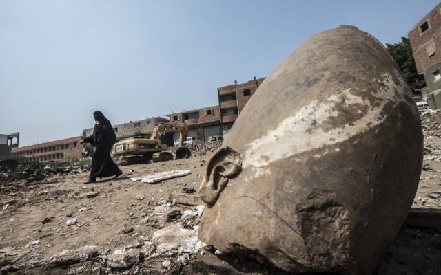An Egyptian woman walks past the head of a statue at the site of a new discovery by a team of German-Egyptian archeologists in Cairo's Mattarya district on March 9, 2017. AFP/KHALED DESOUKI)