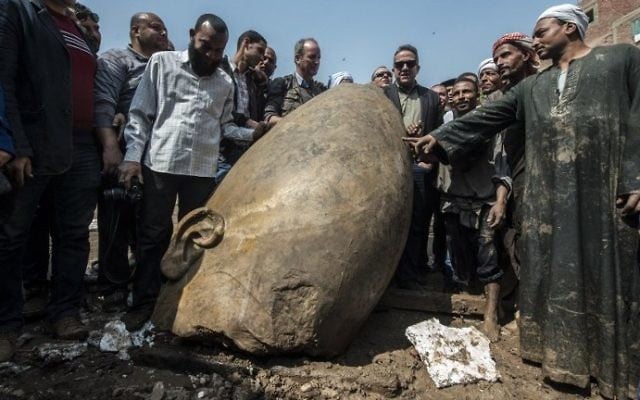 Egyptians pose for pictures next to the head of a statue at the site of a new discovery by a team of German-Egyptian archeologists in Cairo's Mattarya district on March 9, 2017. (AFP/Khaled Desouki)