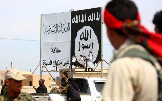 Members of the US-backed Syrian Democratic Forces (SDF), made up of an alliance of Arab and Kurdish fighters, stand under an Islamic State (IS) banner in the recently recaptured Syrian town of Al-Karamah, as they advance to encircle the jihadists' stronghold on Raqqa, on March 26, 2017. (AFP Photo/Delil Souleiman)