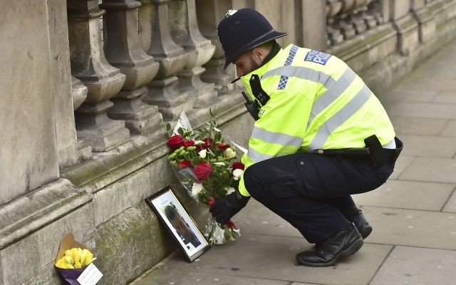 A police officer places flowers and a photo of fellow police officer Keith Palmer, who was killed in yesterdays attack, on Whitehall near the Houses of Parliament in London, Thursday March 23, 2017. (Dominic Lipinski/PA via AP)