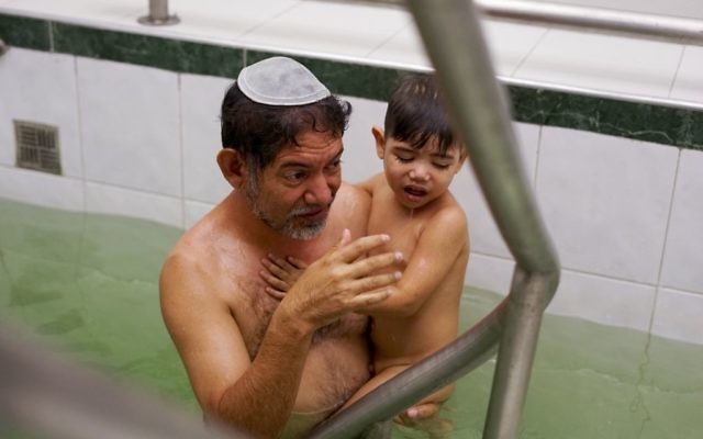 In this March 19, 2017 photo, Franklin Perez dips his son in a special bath to mark their conversion to Judaism in Bogota, Colombia. (AP Photo/Christine Armario)