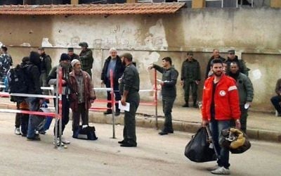 In this photo released by the Syrian official news agency SANA, a Syrian opposition gunmen, left, carries their weapon as some family members leave the al-Waer neighborhood bound for a town on the Turkish border, in Homs, Syria, Monday, March 27, 2017. (SANA via AP)