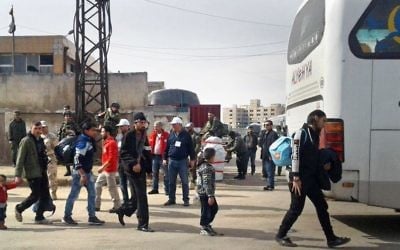 In this photo released by the Syrian official news agency SANA, a Syrian opposition gunman, center left, carries his weapon as some family members leave the al-Waer neighborhood bound for a town on the Turkish border, in Homs, Syria, Monday, March 27, 2017. (SANA via AP)