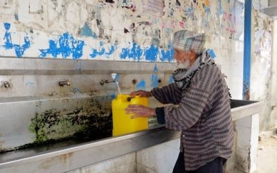 An elderly Palestinian man fills a water container at a public tap at the Khan Yunis Water Authority’s wastewater treatment plant. (CC-BY-4.0 Muhammad Sabah B’Tselem/Wikipedia)