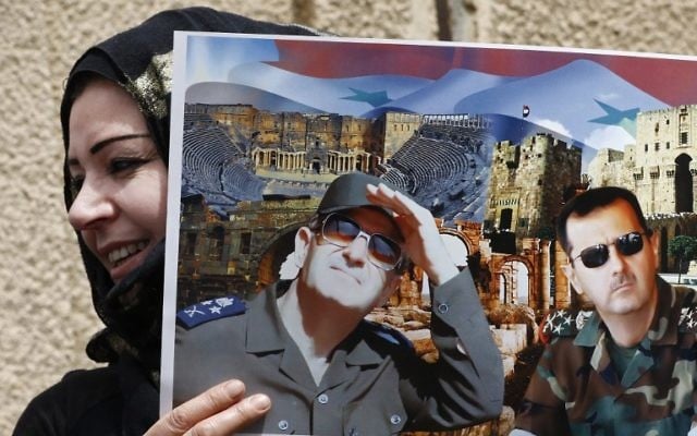 A Syrian protester holds a poster bearing images of the Syrian President (R) and his late father and former president of Syria during a demonstration in support of the governing family outside the United Nation's (UN) office in the capital Damascus on April 8, 2017. (AFP PHOTO / Louai Beshara)