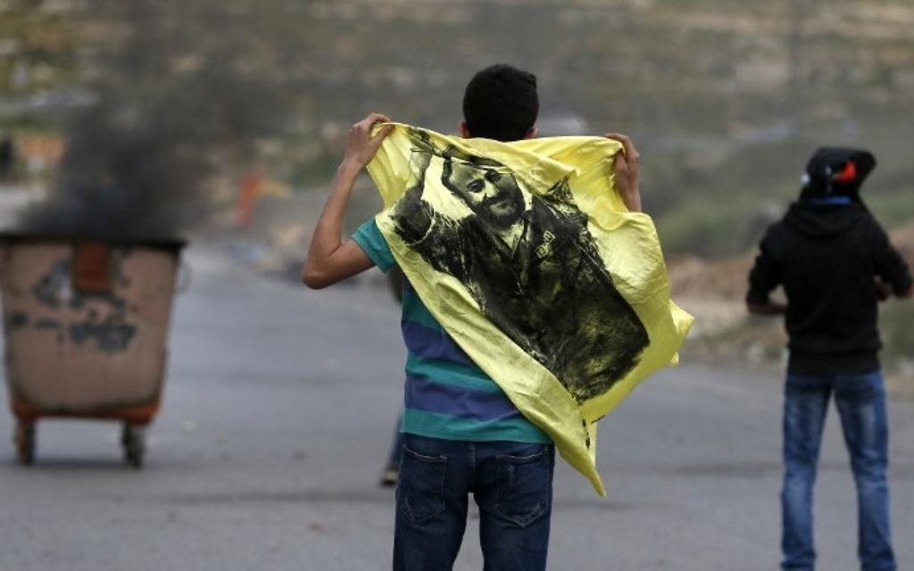 A Palestinian demonstrator holds a flag bearing an image of Marwan Barghouti during a protest near the West Bank settlement of Beit El, north of Ramallah on April 23, 2017. (AFP Photo/Abbas Momani)