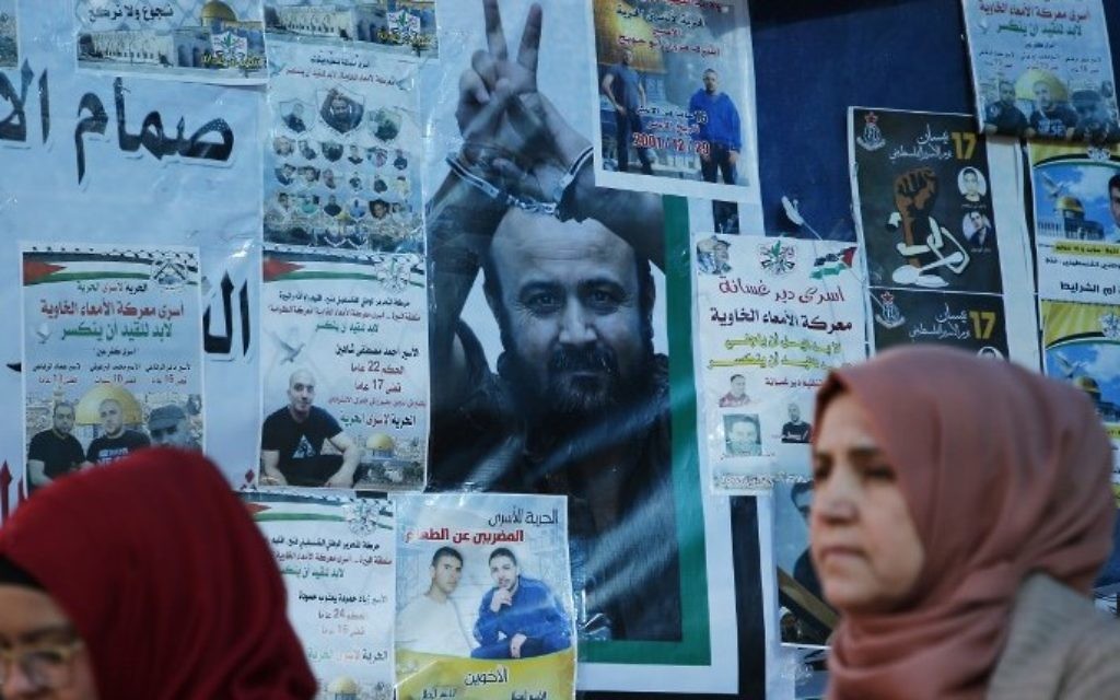 Palestinian women walk past a wall bearing posters, including a portrait of prominent prisoner Marwan Barghouti, during a rally in Ramallah, in support of him and other prisoners on hunger strike in Israeli jails on April 24, 2017. (AFP/Abbas Momani)