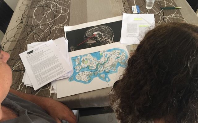 G and S, the parents of alleged bomb hoaxer M, at their home in Ashkelon, with medical documents, one of the maps drawn by M, and an MRI of his brain, on the table in front of them, April 26, 2017 (DH/Times of Israel staff)