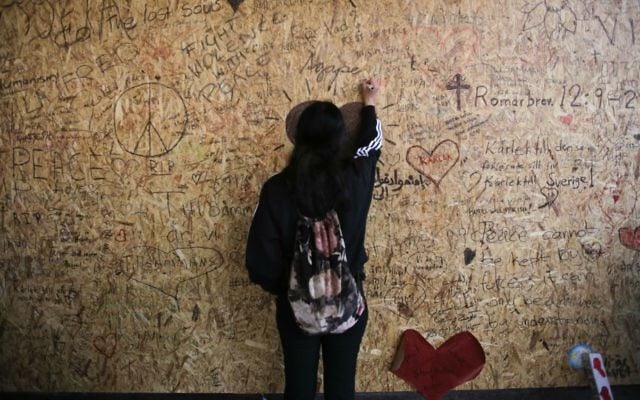 A woman writes a message on a wooden plank at the department store Ahlens in Stockholm, Sweden, Sunday, April 9, 2017, the site of an apparent terror attack the previous Friday. (AP Photo/Markus Schreiber)