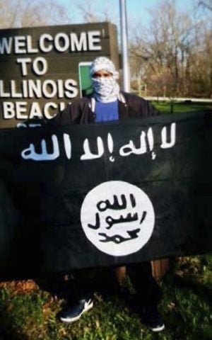 In this undated photo provided by the Federal Bureau of Investigation, Joseph D. Jones poses with an Islamic State group flag at Illinois Beach State Park in Zion, Ill. (FBI via AP)