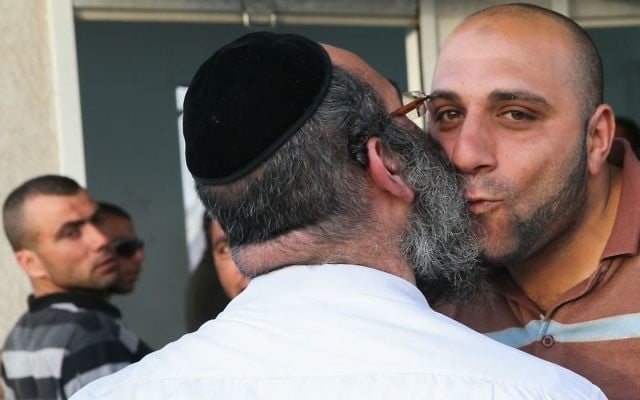 Illustrative image of an ultra-Orthodox Israeli contractor greeting a Palestinian construction worker as he and others wait on the Palestinian side of the checkpoint at the entrance to the West Bank settlement of Beitar Illit. (Nati Shohat/Flash90)