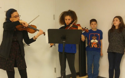 A student and teacher play the violin during a presentation on child victims of the Holocaust at the Midtown Workmen’s Circle School in Manhattan, April 23, 2017. (Ben Sales/JTA)