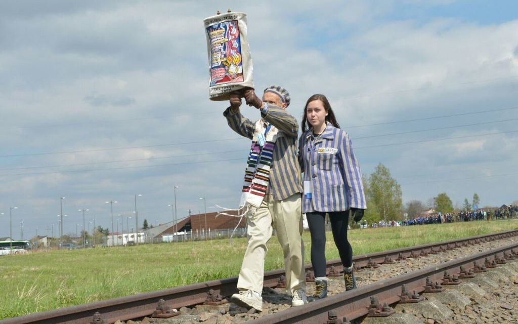 A survivor and his granddaughter walk with a Torah in the March of the Living near Auschwitz-Birkenau on April 24, 2017. (Yossi Zeliger/ Flash90) A survivor and his granddaughter walk with a Torah in the March of the Living near Auschwitz-Birkenau on April 24, 2017. (Yossi Zeliger/ Flash90)