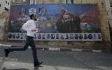 A Palestinian runs past a poster bearing a portrait of convicted terrorist and prominent Palestinian prisoner Marwan Barghouti in the West Bank city of Ramallah on May 3, 2017. (AFP/ ABBAS MOMANI)