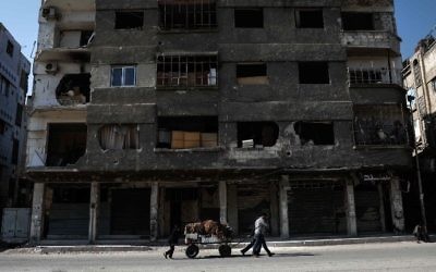 A Syrian street seller pulls a cart of vegetables past a destroyed building in the rebel-held town of Douma, on the eastern outskirts of Damascus on May 6, 2017. (Sameer Al-Doumy/AFP)