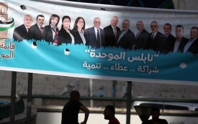 Young men sit on a ledge past campaign posters displaying an electoral list ahead of municipal elections in the northern West Bank city of Nablus, on May 10, 2017. (AFP/Jaafar Ashtiyeh)