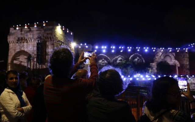 People watch on May 20, 2017, the iconic photo taken by David Rubinger of Israeli paratroopers standing next to the Western Wall on June 1967 during an audio slideshow projected on the ancient walls of Jerusalem's Old City on the beginning of the week marking the 50th anniversary of the 1967 Israeli-Arab War.  (AFP PHOTO / GALI TIBBON)