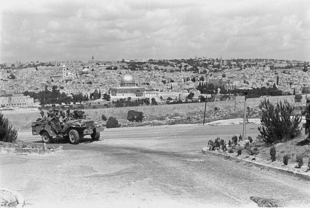 Paratroopers ride in a jeep near the East Jerusalem neighborhood of A-Tur, with the Old City of Jerusalem behind them, on June 5, 1967. (Amos Zucker/Bamahane Magazine/Defense Ministry's IDF Archive) Paratroopers ride in a jeep near the East Jerusalem neighborhood of A-Tur, with the Old City of Jerusalem behind them, on June 5, 1967. (Amos Zucker/Bamahane Magazine/Defense Ministry's IDF Archive)